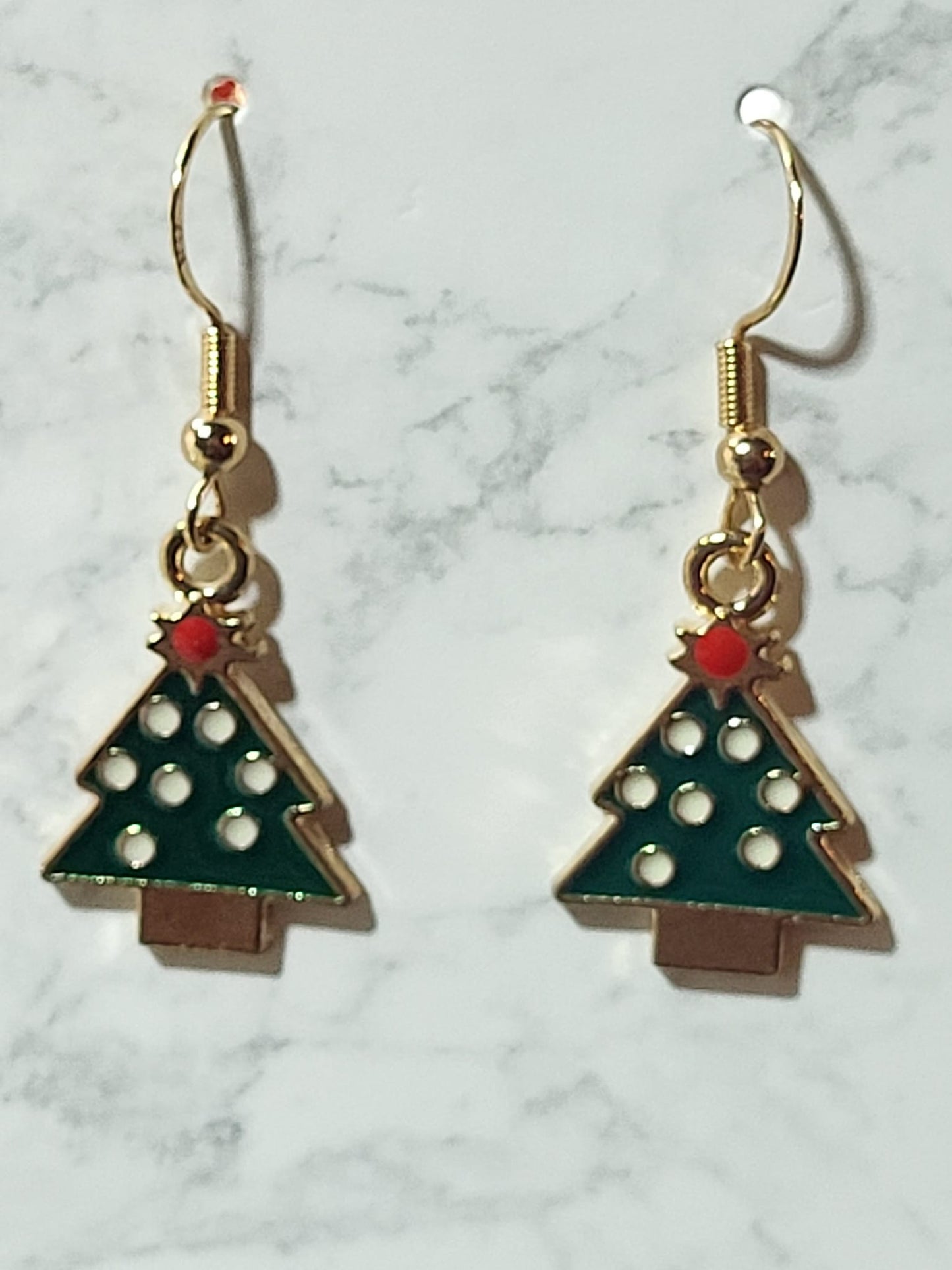 Dark green enamel geometric Christmas tree dangle earrings with white polka dot ornaments, brown trunk and red bead topper on gold French wire on marble surface