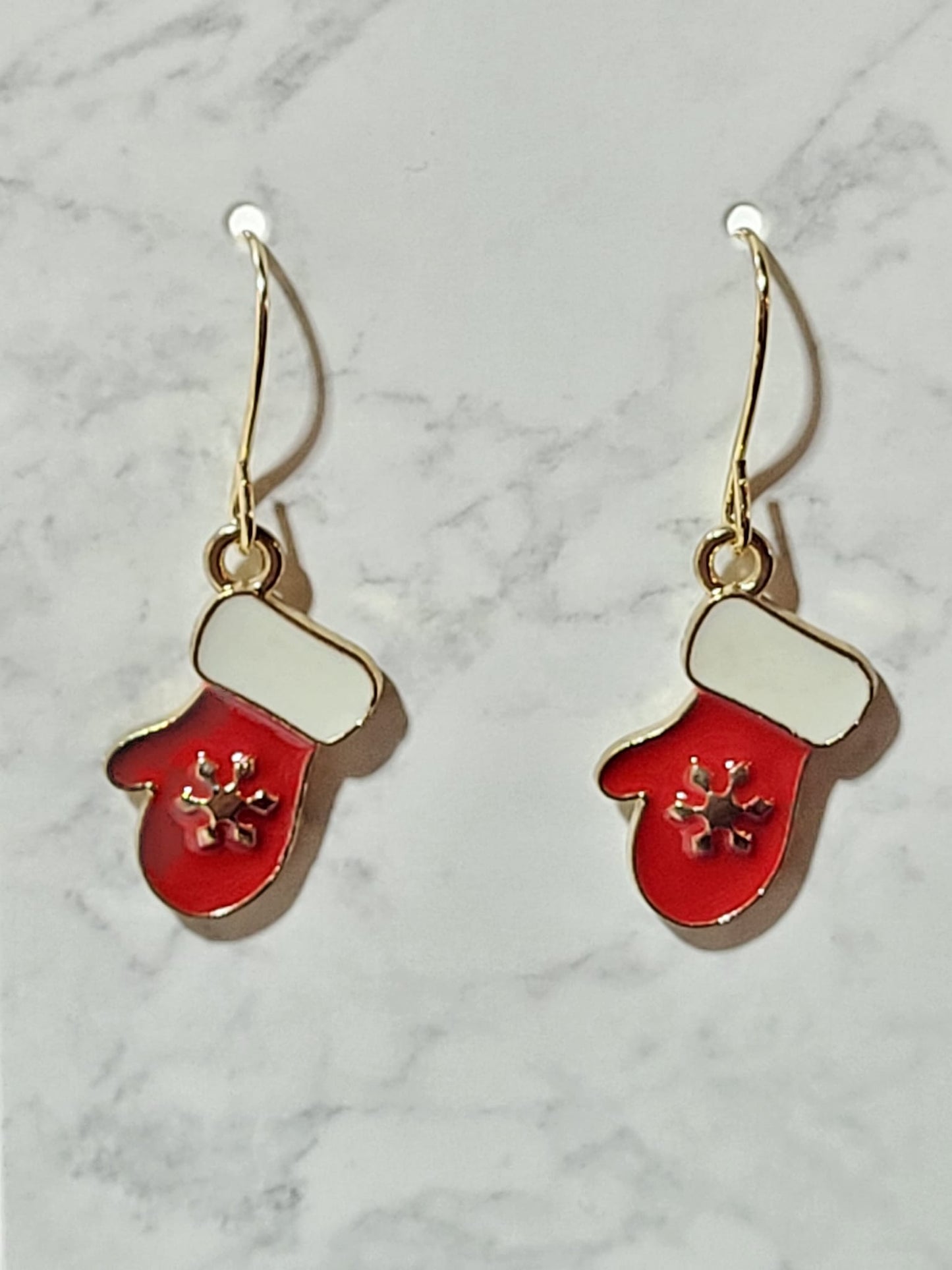 Red enamel mitten charm dangle earrings with white cuff and gold snowflake cutout detail on gold French wire on marble surface