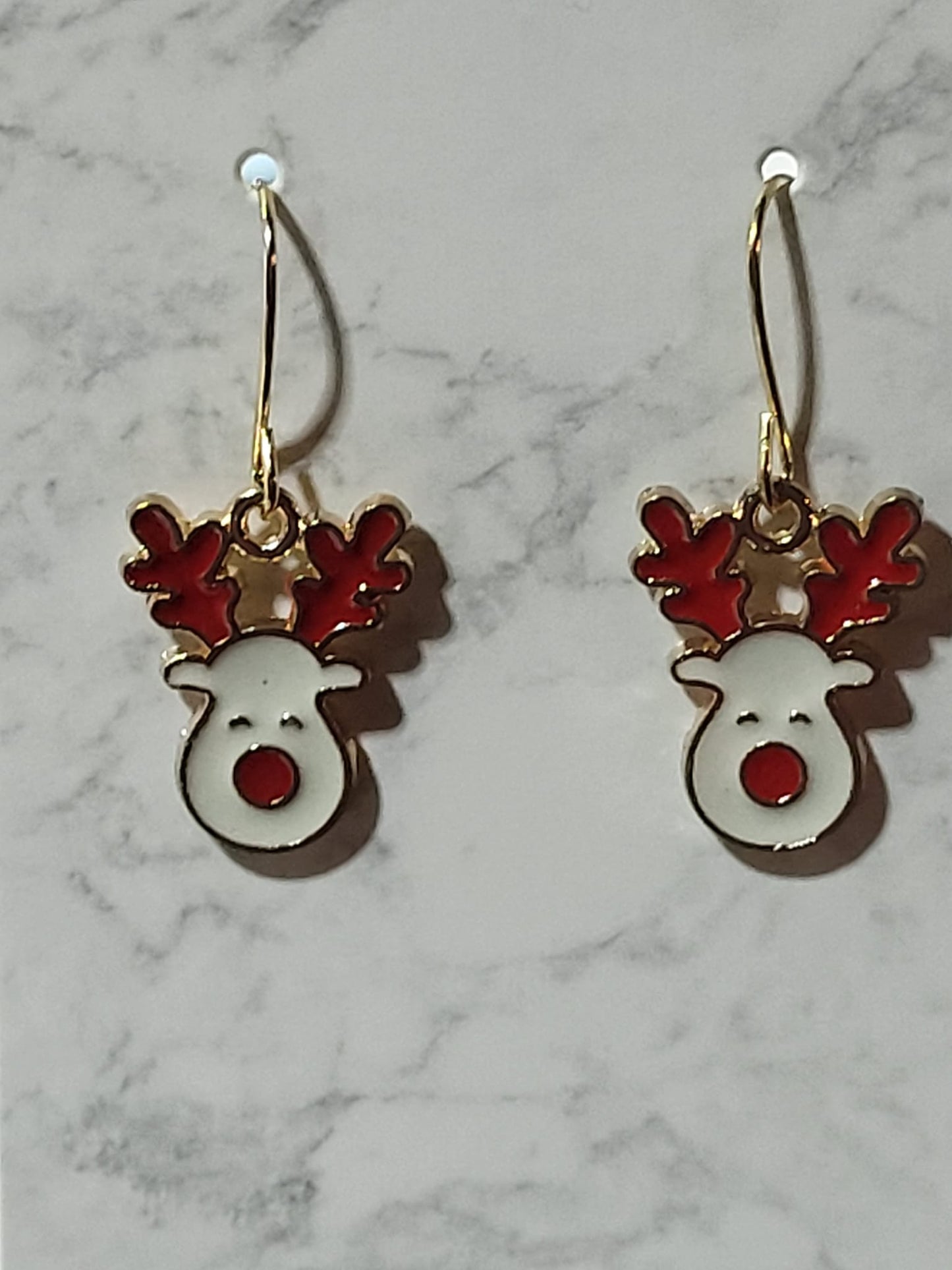 White enamel Rudolph reindeer face dangle earrings with red antlers and big red nose on gold French wire on marble surface