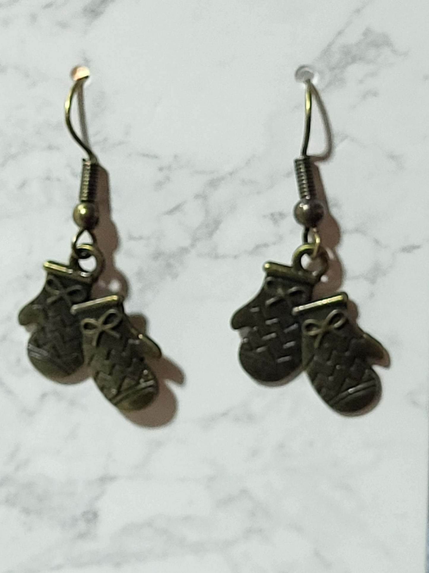Antique bronze double mitten charm dangle earrings with knit texture and bow detail on bronze French wire on marble surface