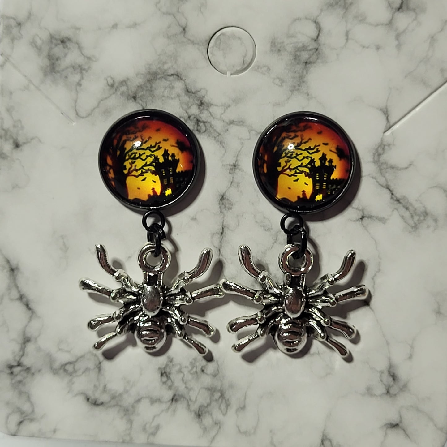 Haunted house spider drop earrings on marble card showing round glass dome cab stud with orange Halloween scene and silver spider charm pendant