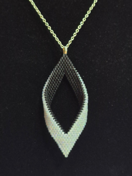 Alternate view of the black and white open leaf pendant hanging from a gold-tone chain.