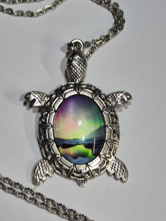 Silver-tone turtle necklace with green and purple northern lights imagery on a white surface.