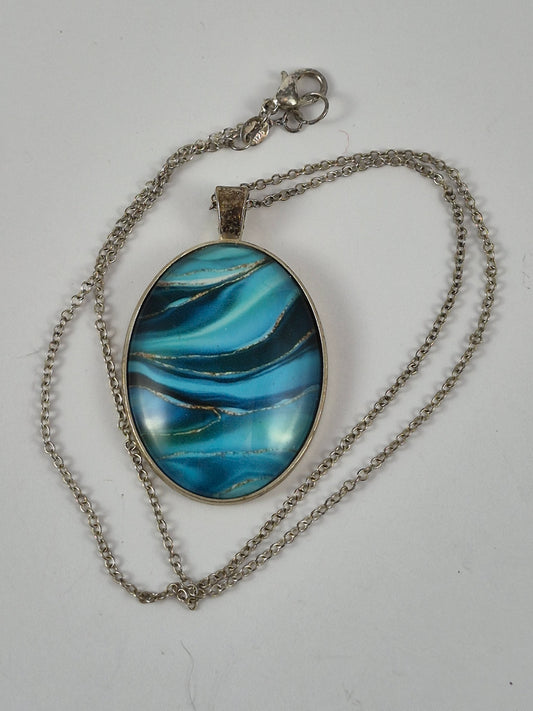 Blue swirl oval pendant necklace and silver-tone chain laid out on a pale background.