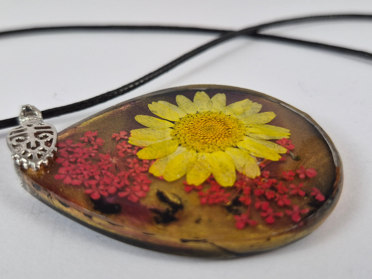 Angled view of the glossy floral resin pendant with decorative silver-tone bail and black cord.