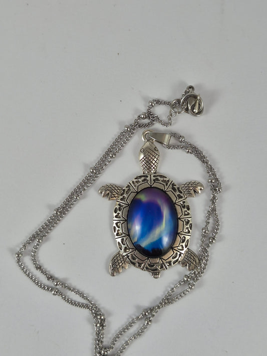 Deep blue aurora sea turtle pendant necklace and chain laid out on a pale background.
