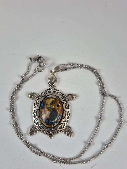 Blue and gold-toned sea turtle pendant necklace and chain laid out on a pale background.
