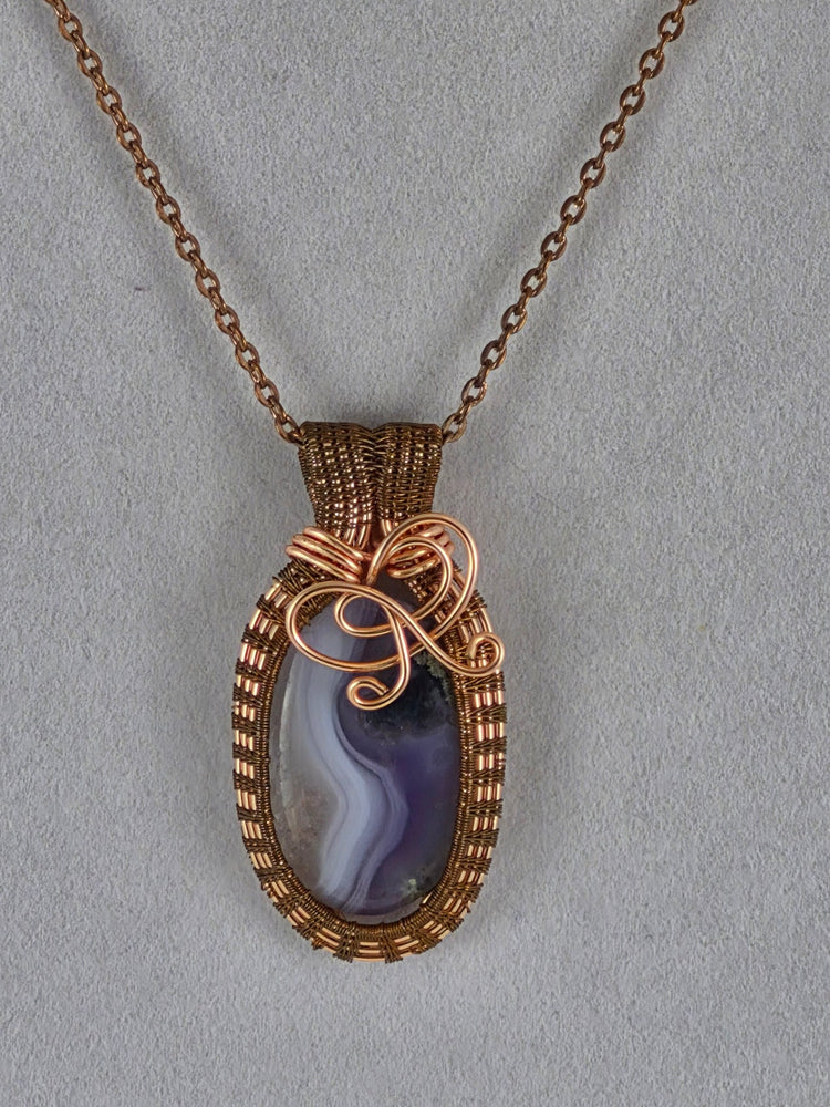 Purple and white banded oval pendant framed by copper-colored woven wire and decorative curls.