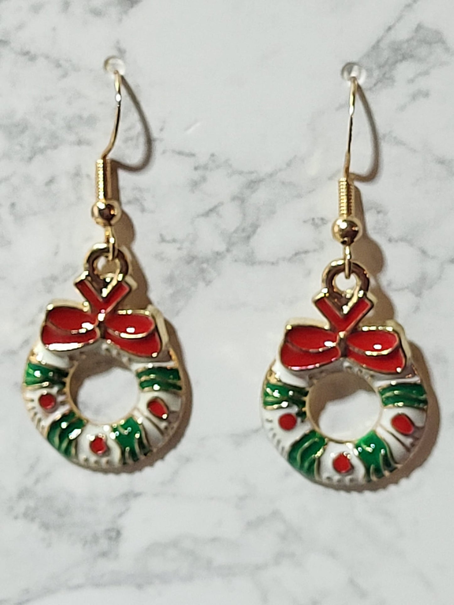 Enamel Christmas wreath charm dangle earrings with red bow, green holly branches and red berry dots on gold French wire on marble surface