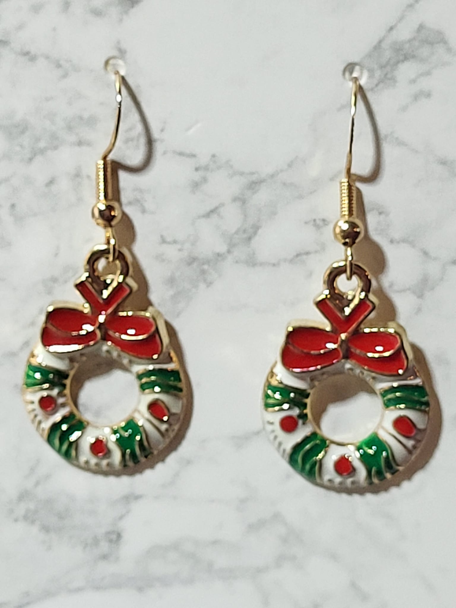 Enamel Christmas wreath charm dangle earrings with red bow, green holly branches and red berry dots on gold French wire on marble surface