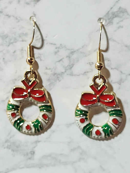 Enamel Christmas wreath charm dangle earrings with red bow, green holly branches and red berry dots on gold French wire on marble surface