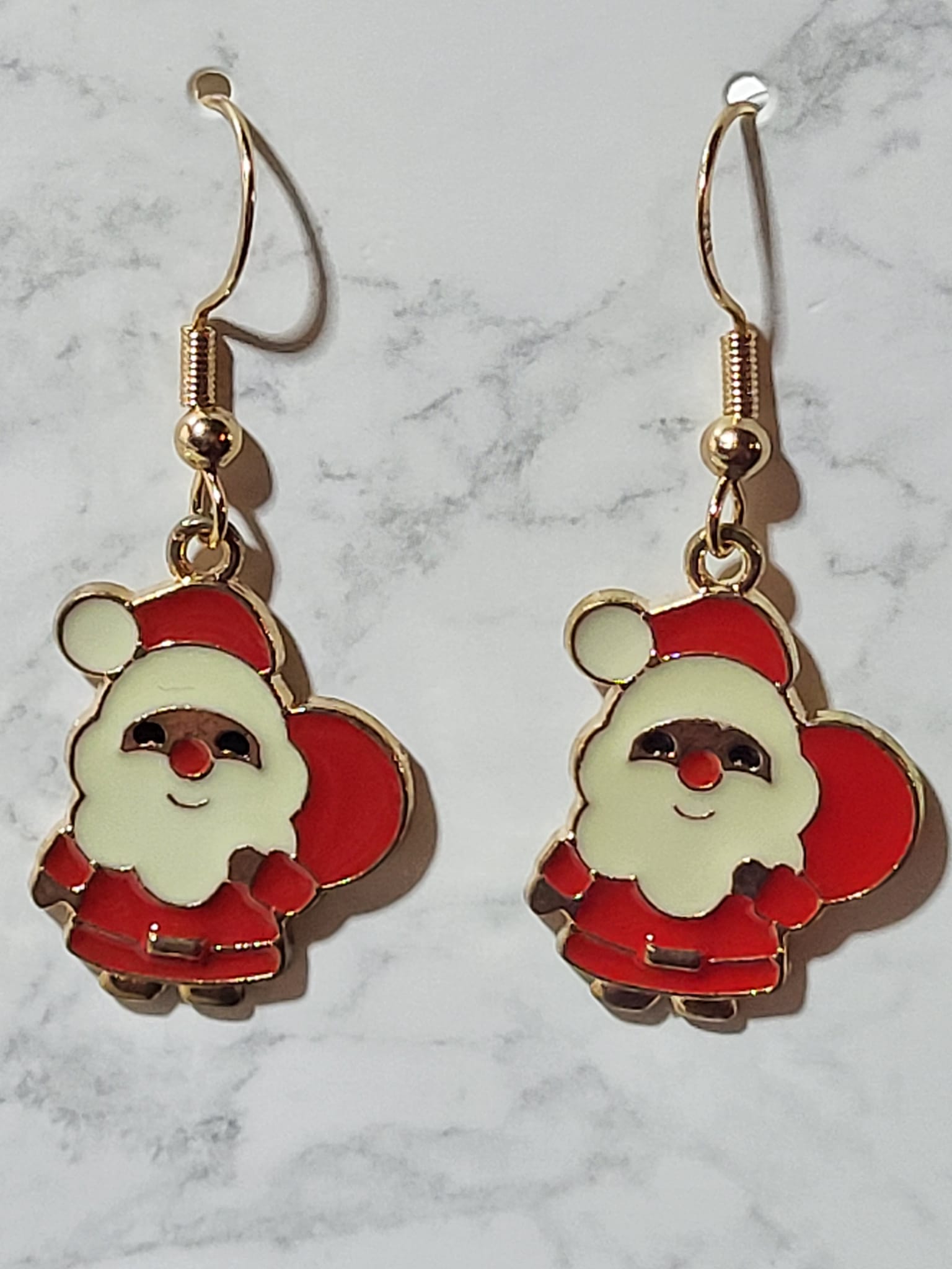 Full body Santa Claus enamel charm dangle earrings with red suit, smiling face and gift sack on gold French wire on marble surface