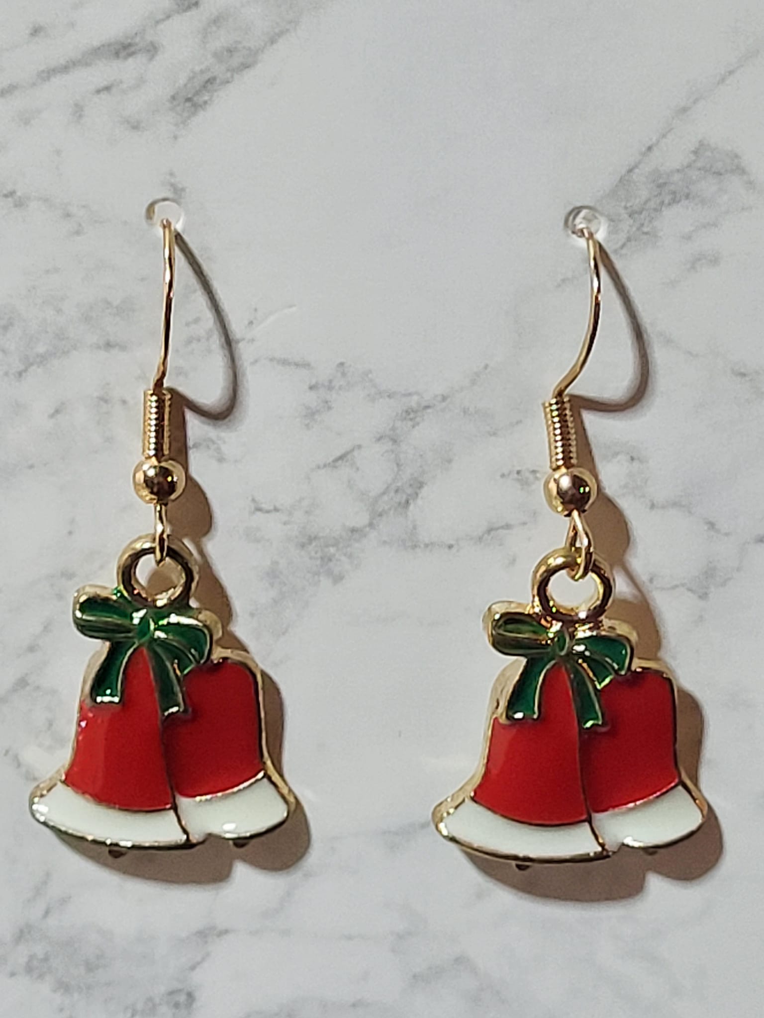 Red and white enamel double jingle bell dangle earrings with green enamel bow and gold tone outline on gold French wire on marble surface