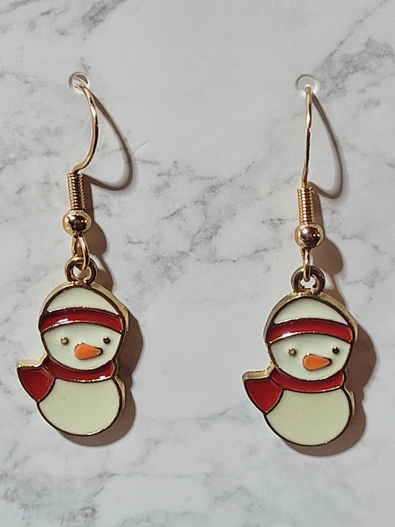 Enamel snowman charm dangle earrings with red scarf and hat band, orange carrot nose and gold tone outline on gold French wire on marble surface
