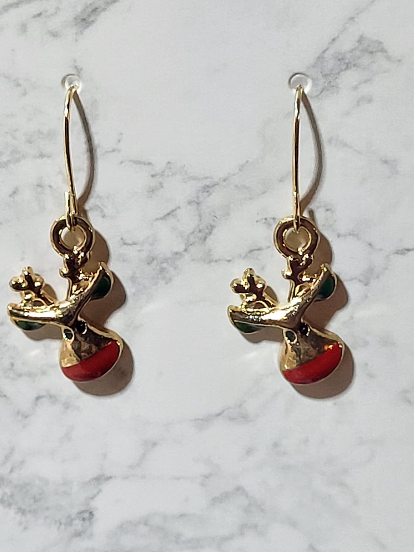 Gold tone Rudolph reindeer face charm dangle earrings with detailed antlers and glossy red nose on gold French wire on marble surface