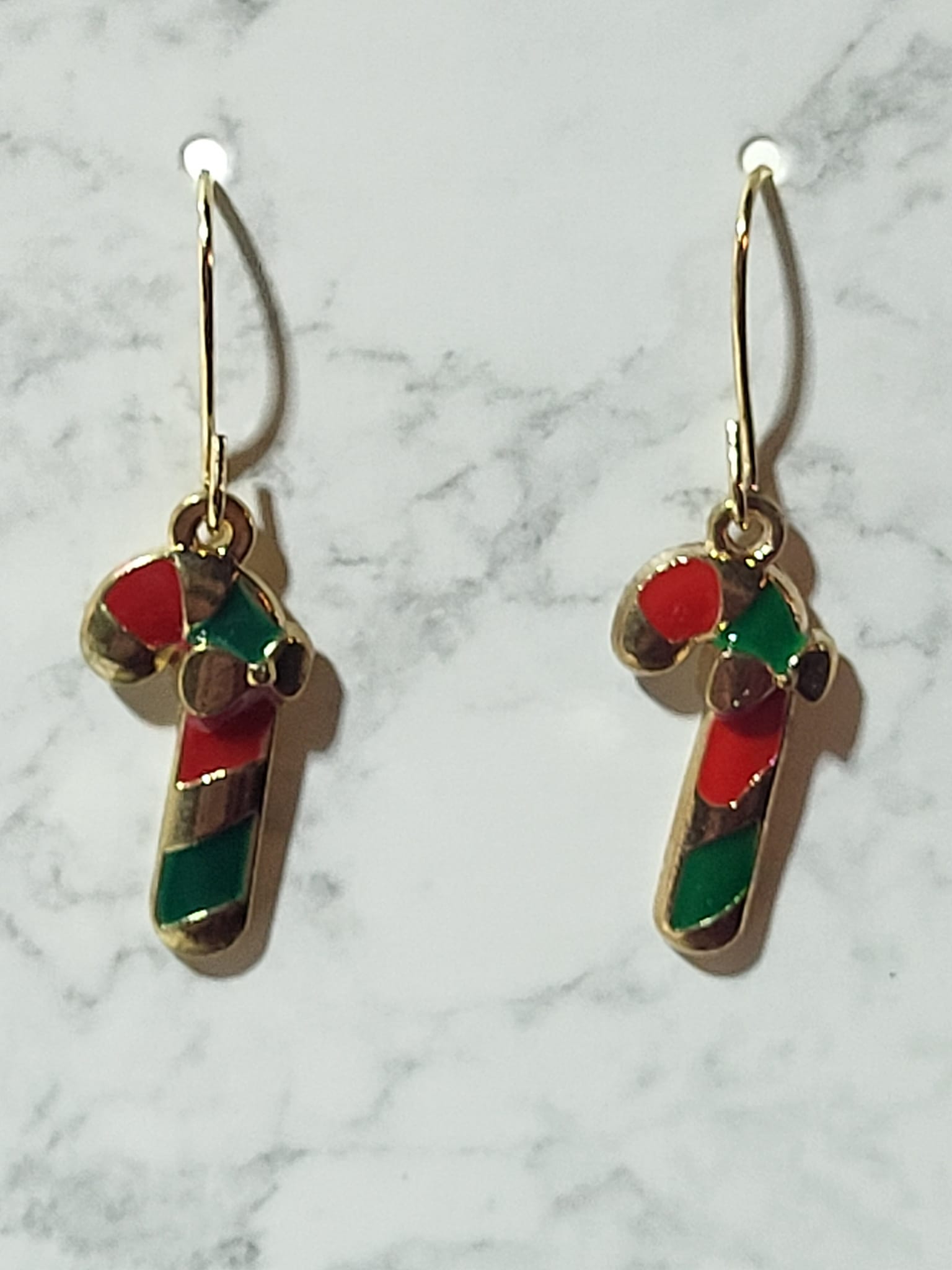 Red and green enamel candy cane dangle earrings with green bow and gold tone outline on gold French wire on marble surface