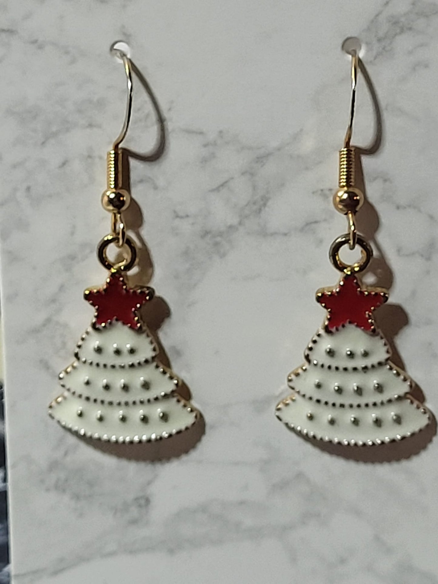 White enamel Christmas tree dangle earrings with gold dot tier detail and red enamel star topper on gold French wire on marble surface