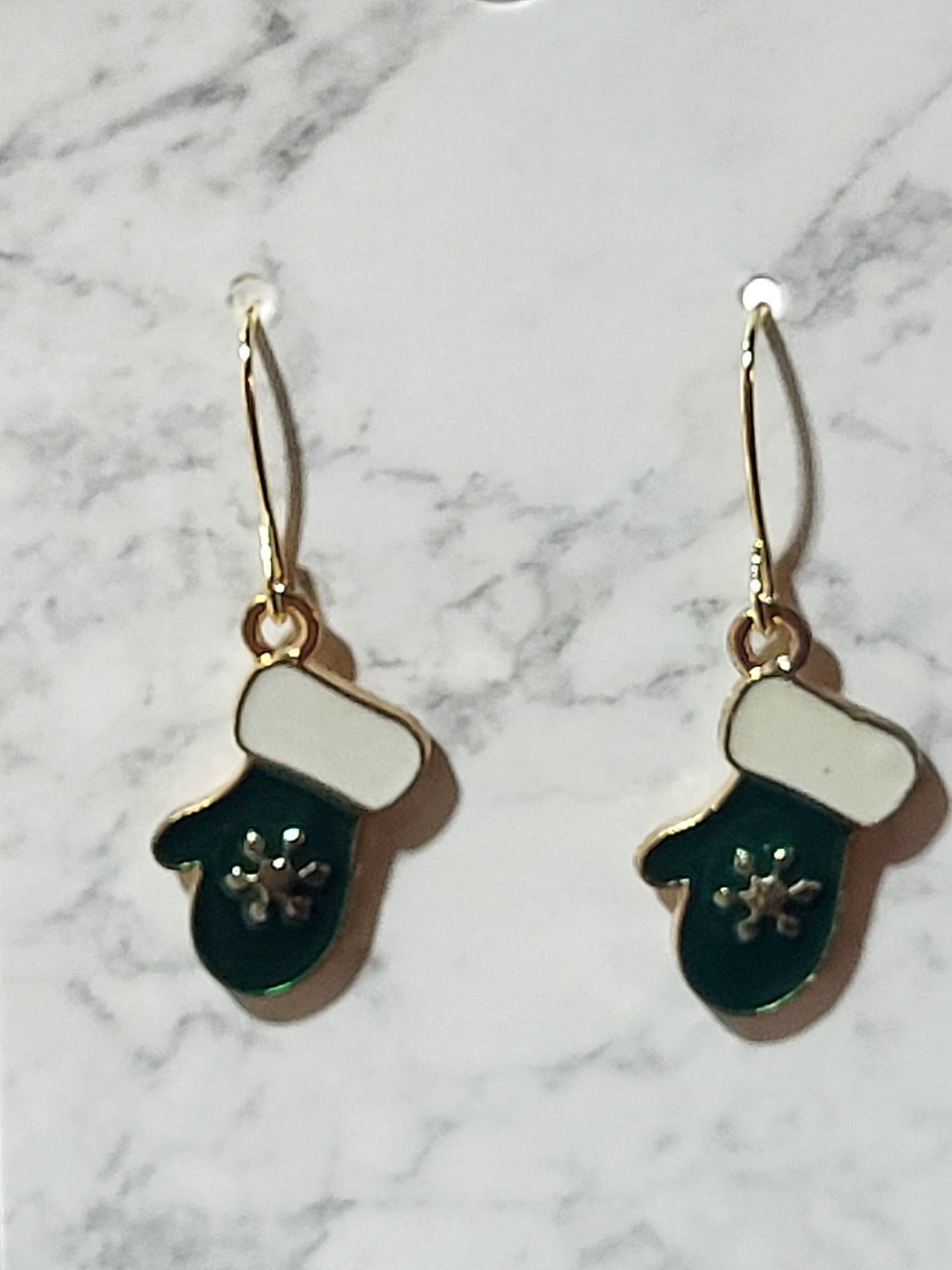 Teal enamel mitten dangle earrings with white cuff and silver snowflake on gold ear wire on marble surface