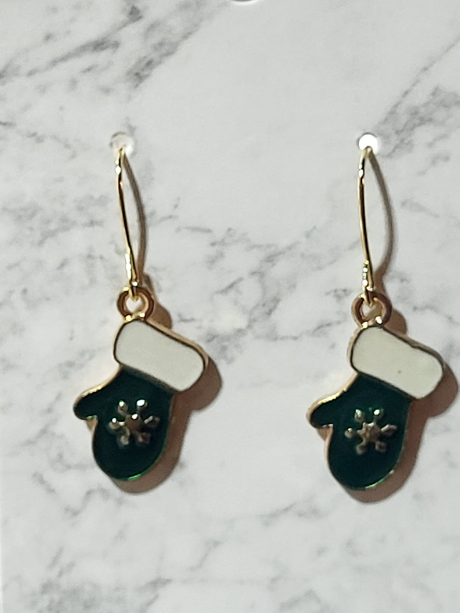 Teal enamel mitten dangle earrings with white cuff and silver snowflake on gold ear wire on marble surface