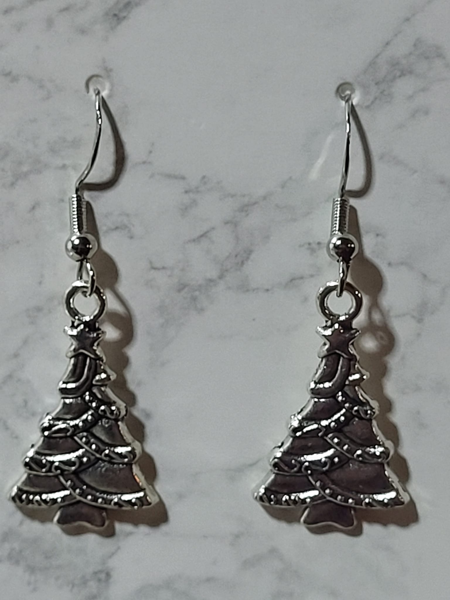 Antique silver Christmas tree charm dangle earrings with star topper and garland detail on silver French wire on marble surface