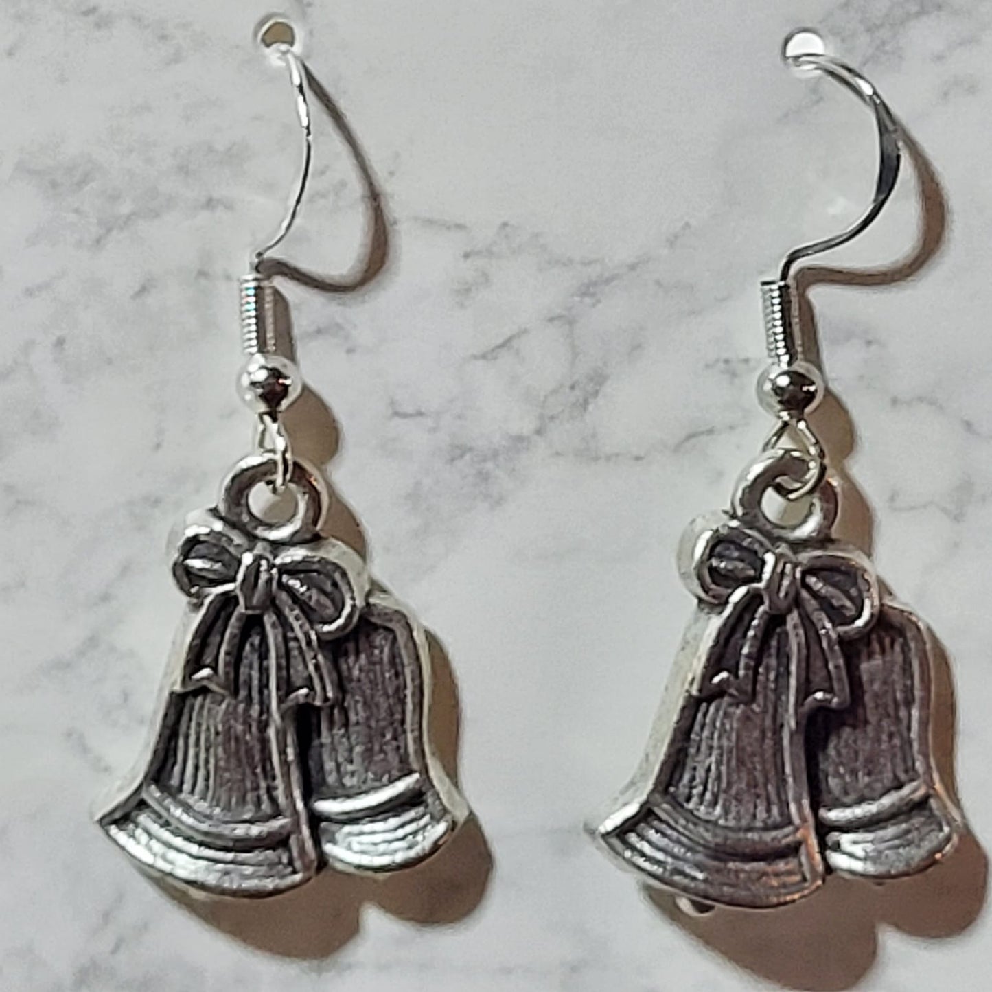 Antique silver double jingle bell charm dangle earrings with bow detail on silver French wire on marble surface