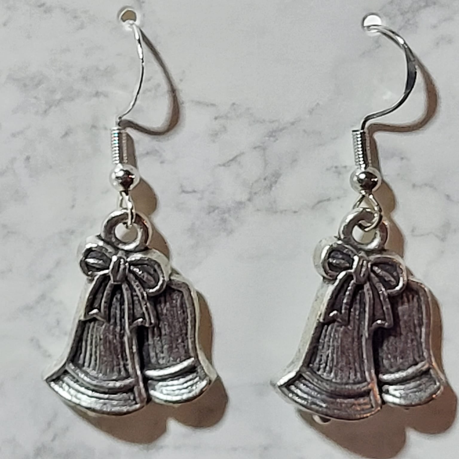 Antique silver double jingle bell charm dangle earrings with bow detail on silver French wire on marble surface