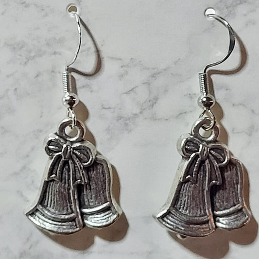 Antique silver double jingle bell charm dangle earrings with bow detail on silver French wire on marble surface