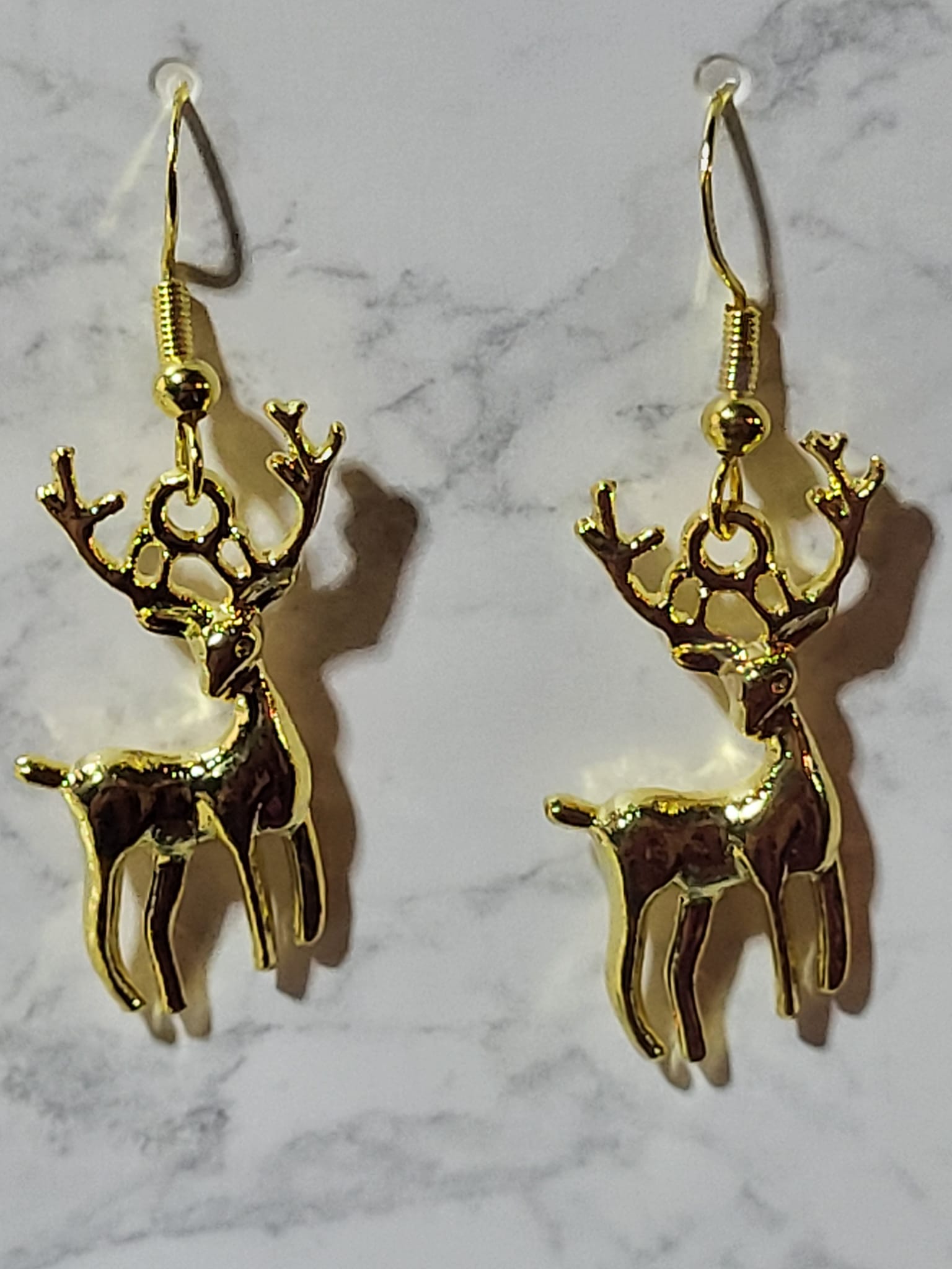 Gold tone full-body reindeer stag charm dangle earrings with detailed antlers on gold French wire on marble surface