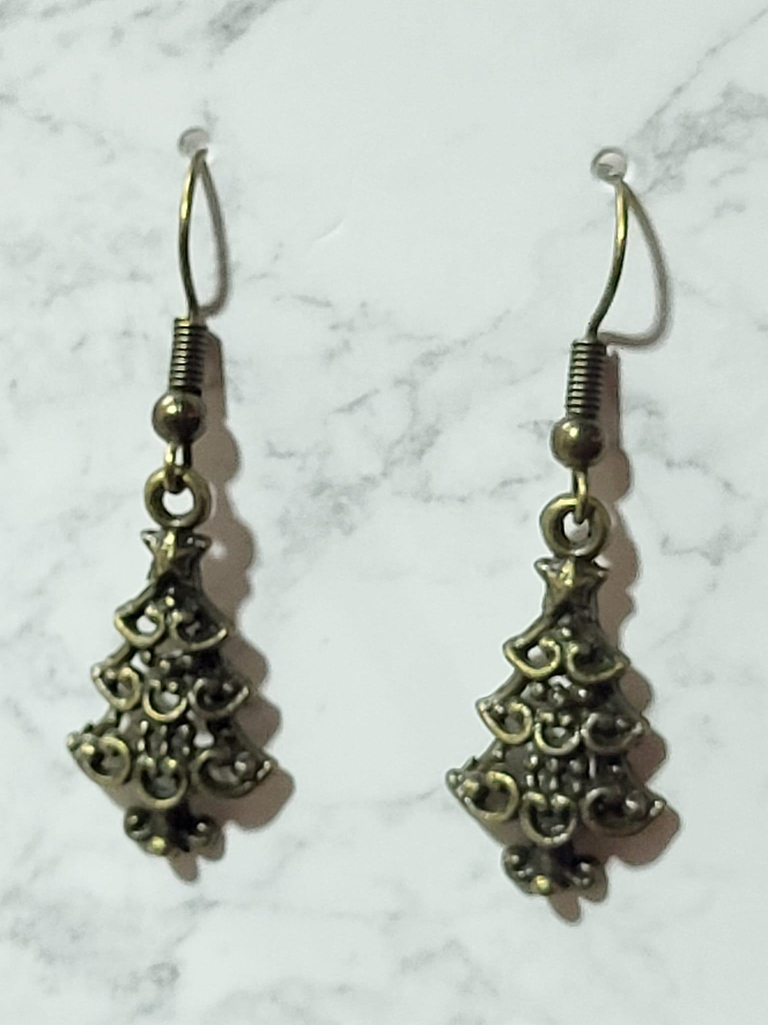 Antique bronze filigree Christmas tree charm dangle earrings with ornate scroll detail on bronze French wire on marble surface
