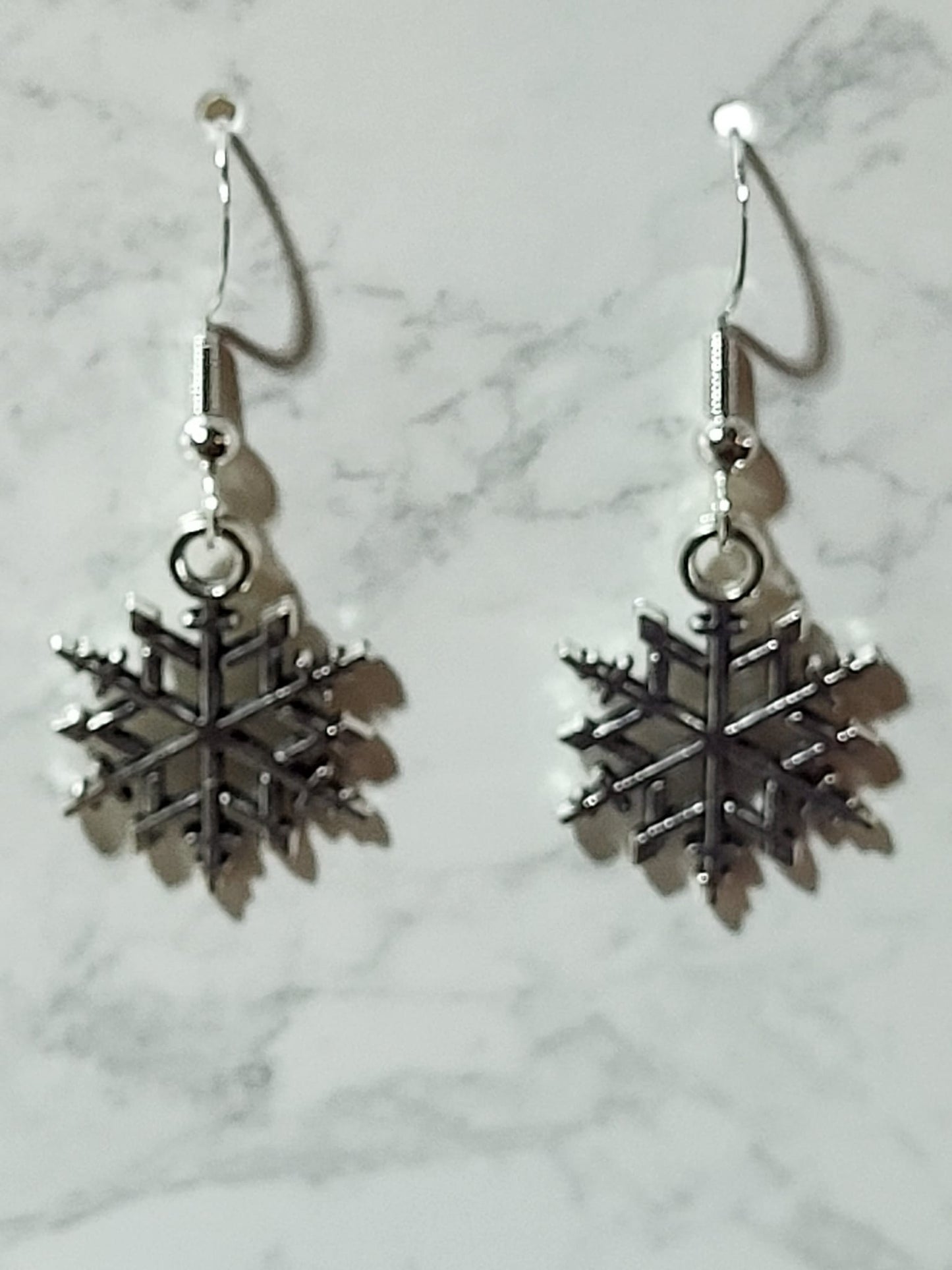 Silver geometric snowflake charm dangle earrings with intricate branch and dot detail on silver French wire on marble surface