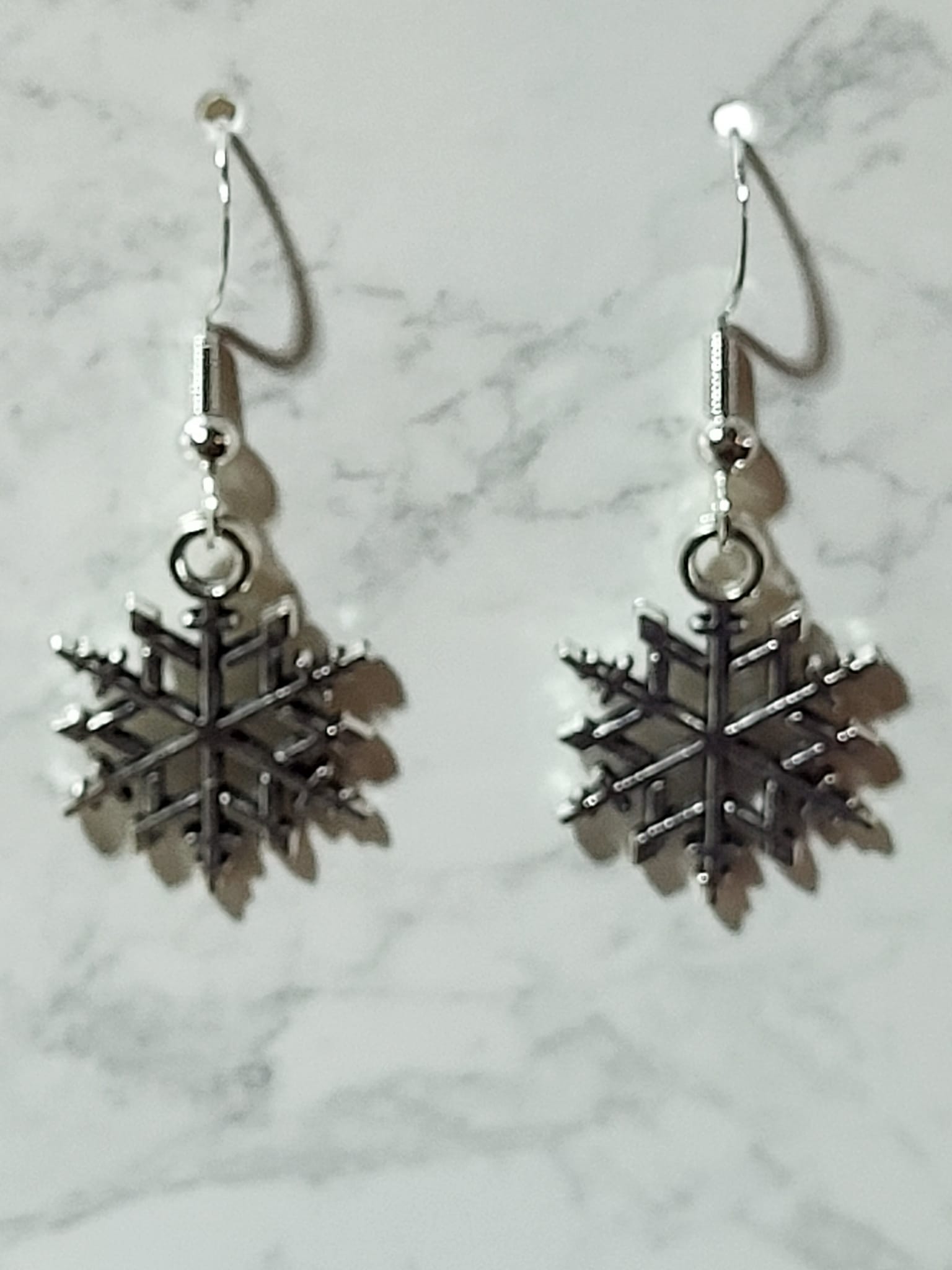Silver geometric snowflake charm dangle earrings with intricate branch and dot detail on silver French wire on marble surface