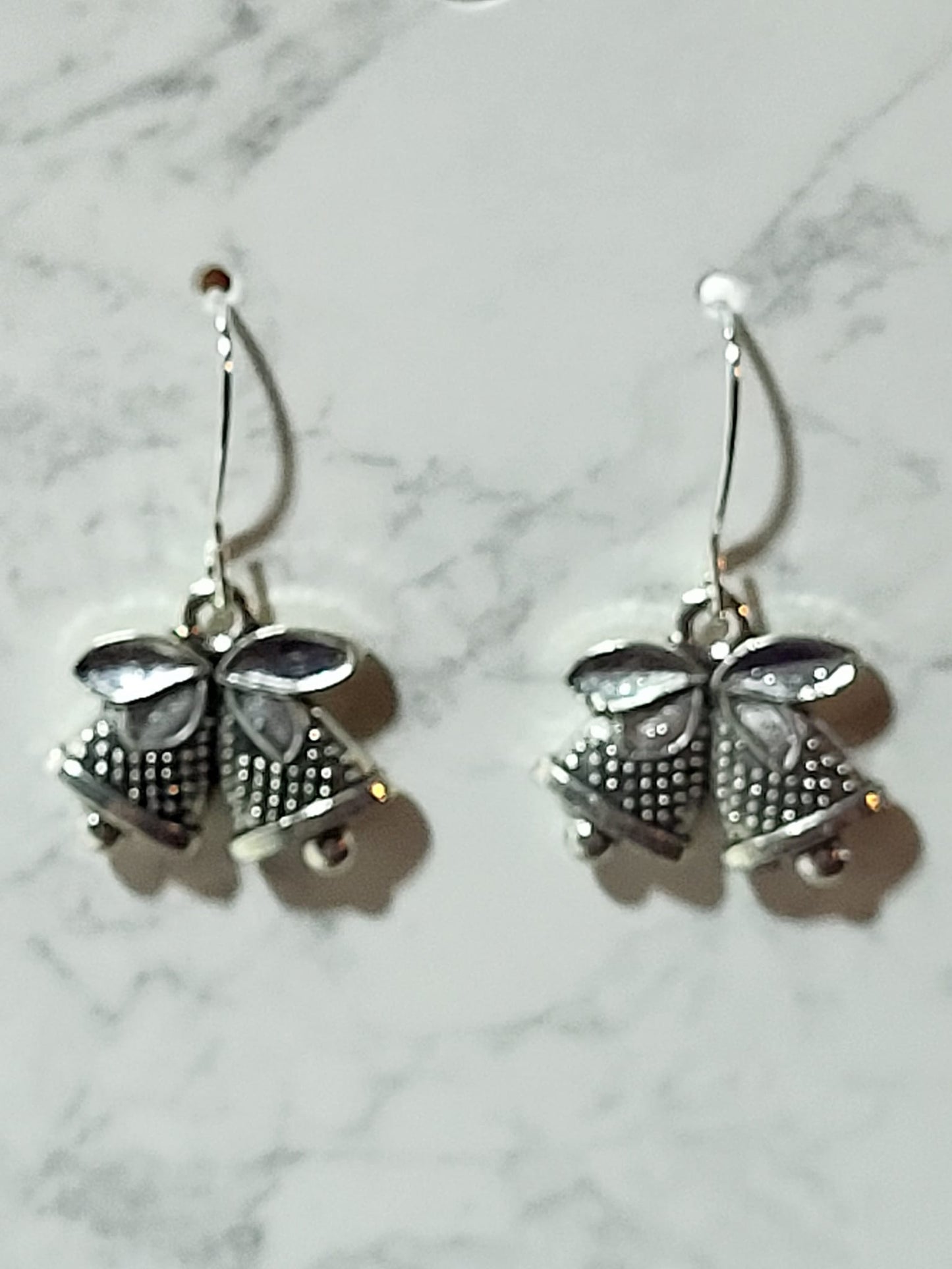Antique silver double jingle bell charm dangle earrings with dotted texture and bow detail on silver French wire on marble surface