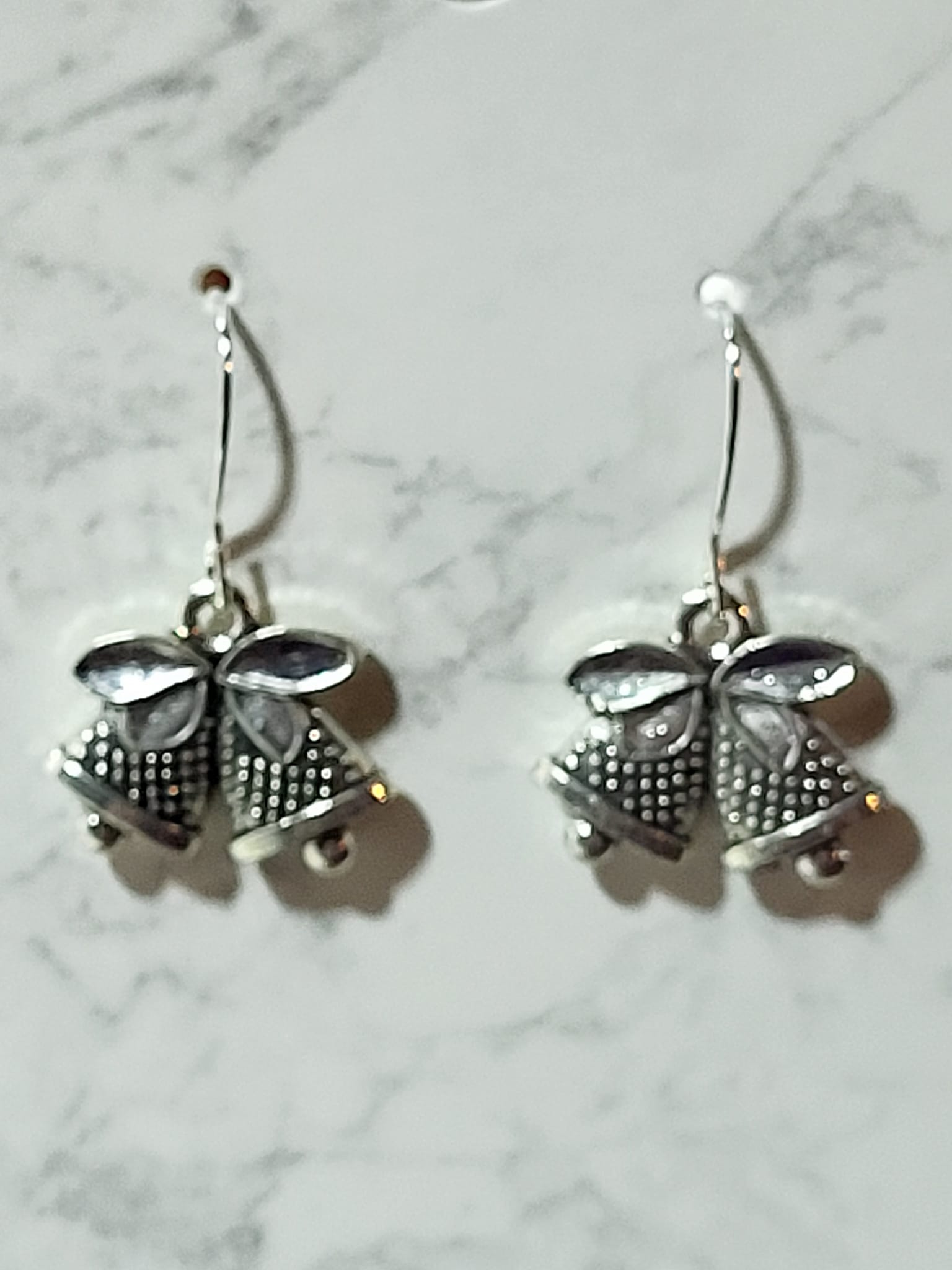 Antique silver double jingle bell charm dangle earrings with dotted texture and bow detail on silver French wire on marble surface