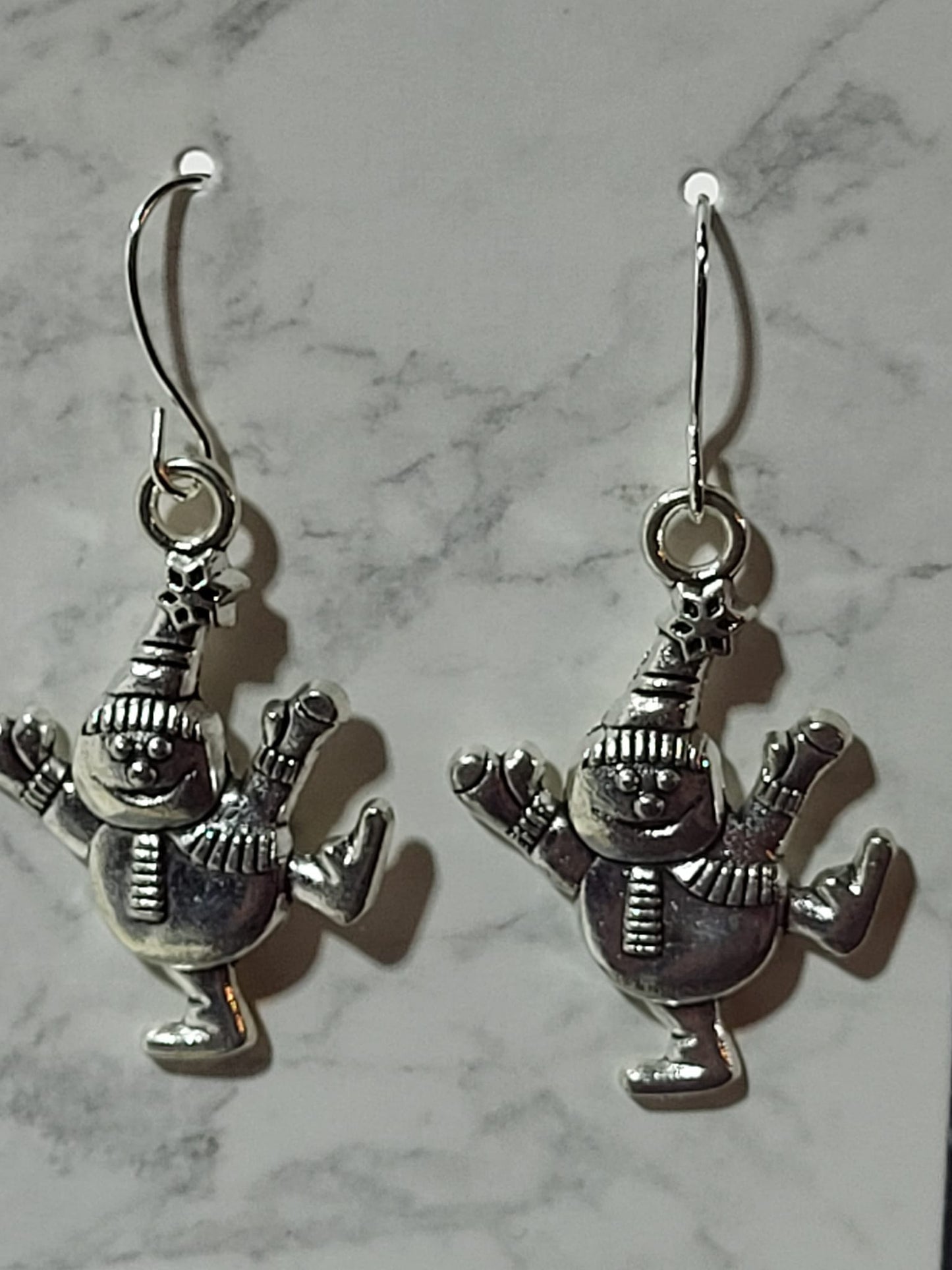Silver dancing snowman charm dangle earrings with pointed hat and striped scarf on silver French wire on marble surface