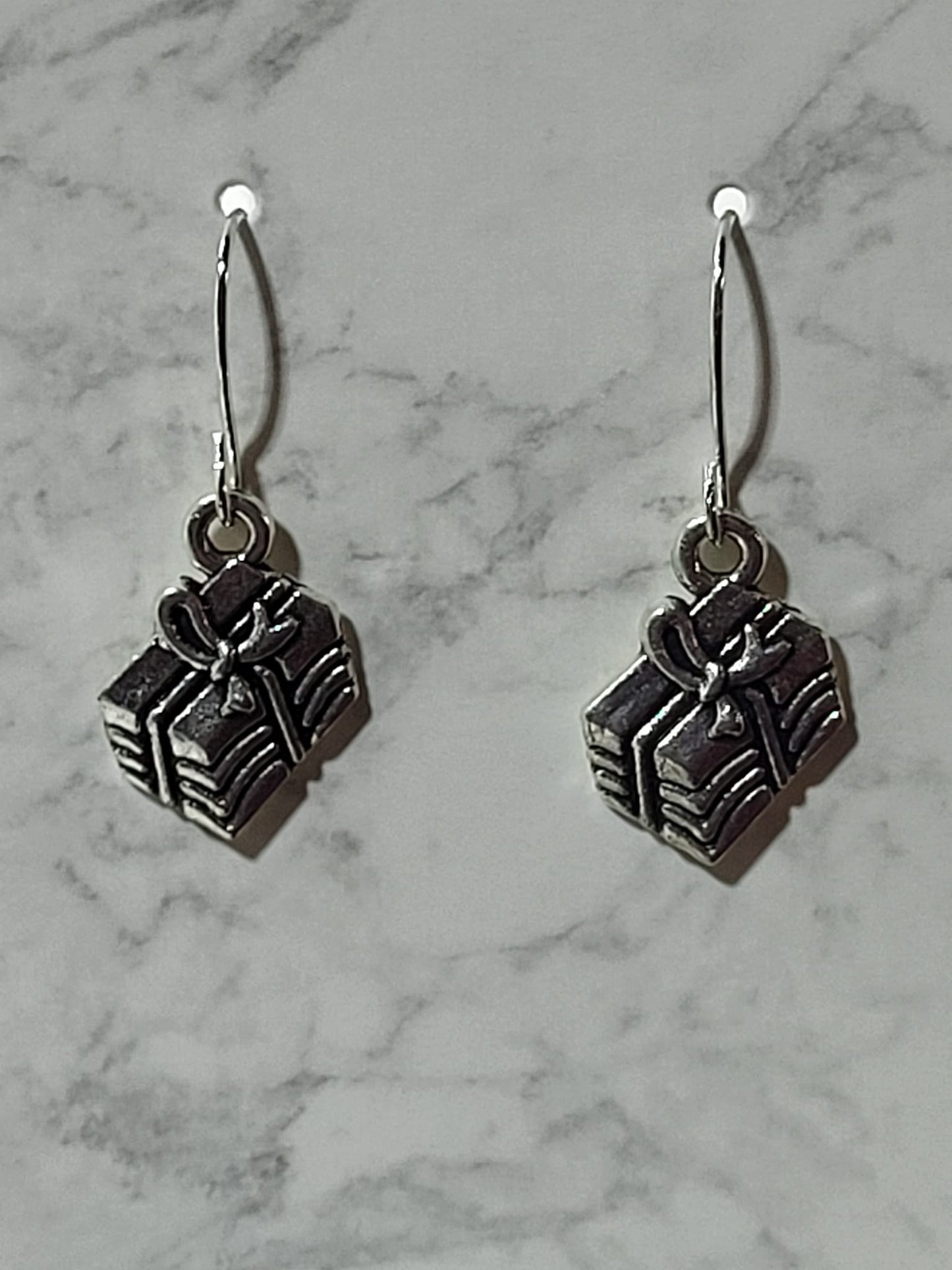 Silver 3D gift box charm dangle earrings with ribbed sides and bow detail on silver French wire on marble surface