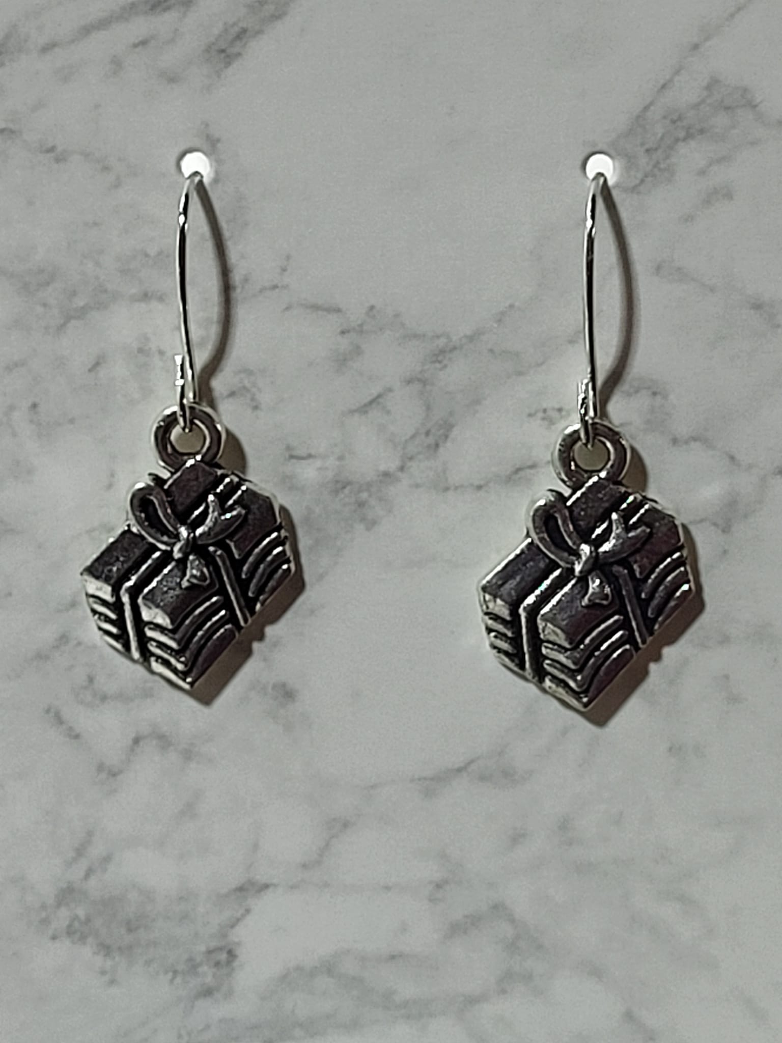 Silver 3D gift box charm dangle earrings with ribbed sides and bow detail on silver French wire on marble surface