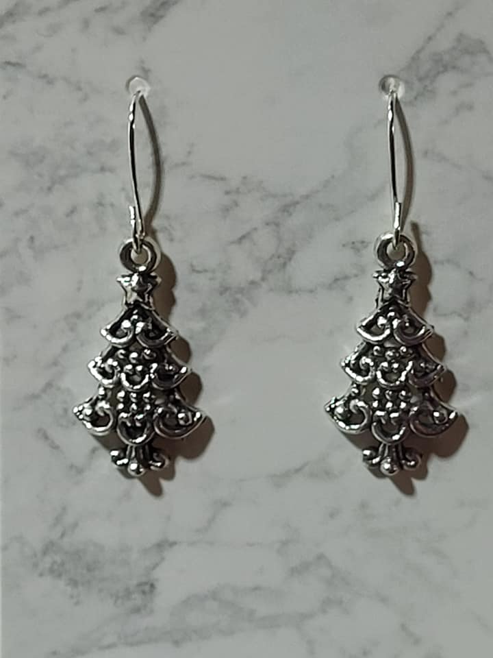 Ornate antique silver filigree Christmas tree charm dangle earrings with tiered scroll detail and star topper on silver French wire on marble surface