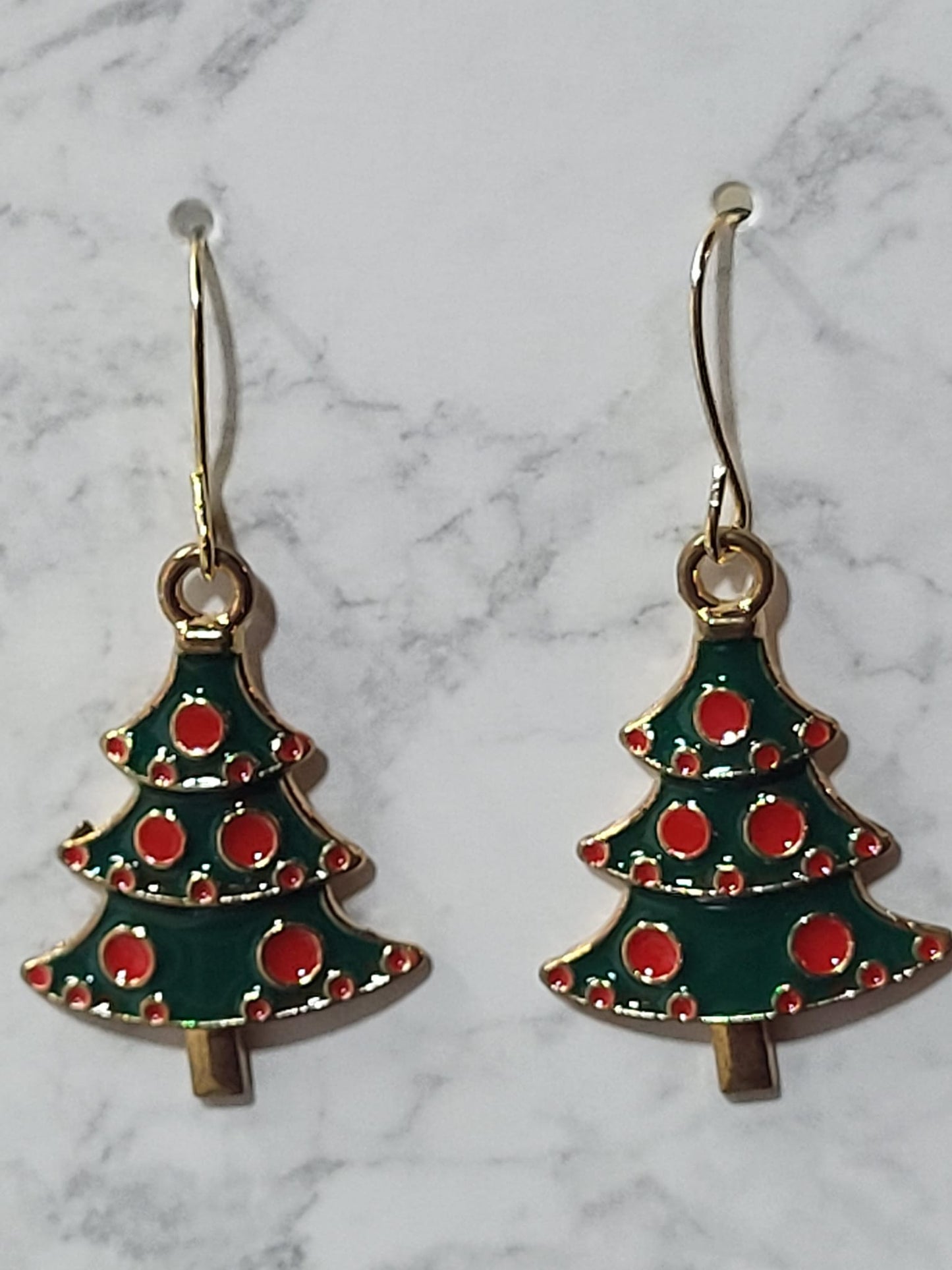 Green and red enamel Christmas tree charm dangle earrings with red ornament dots and gold tone outline on gold French wire on marble surface