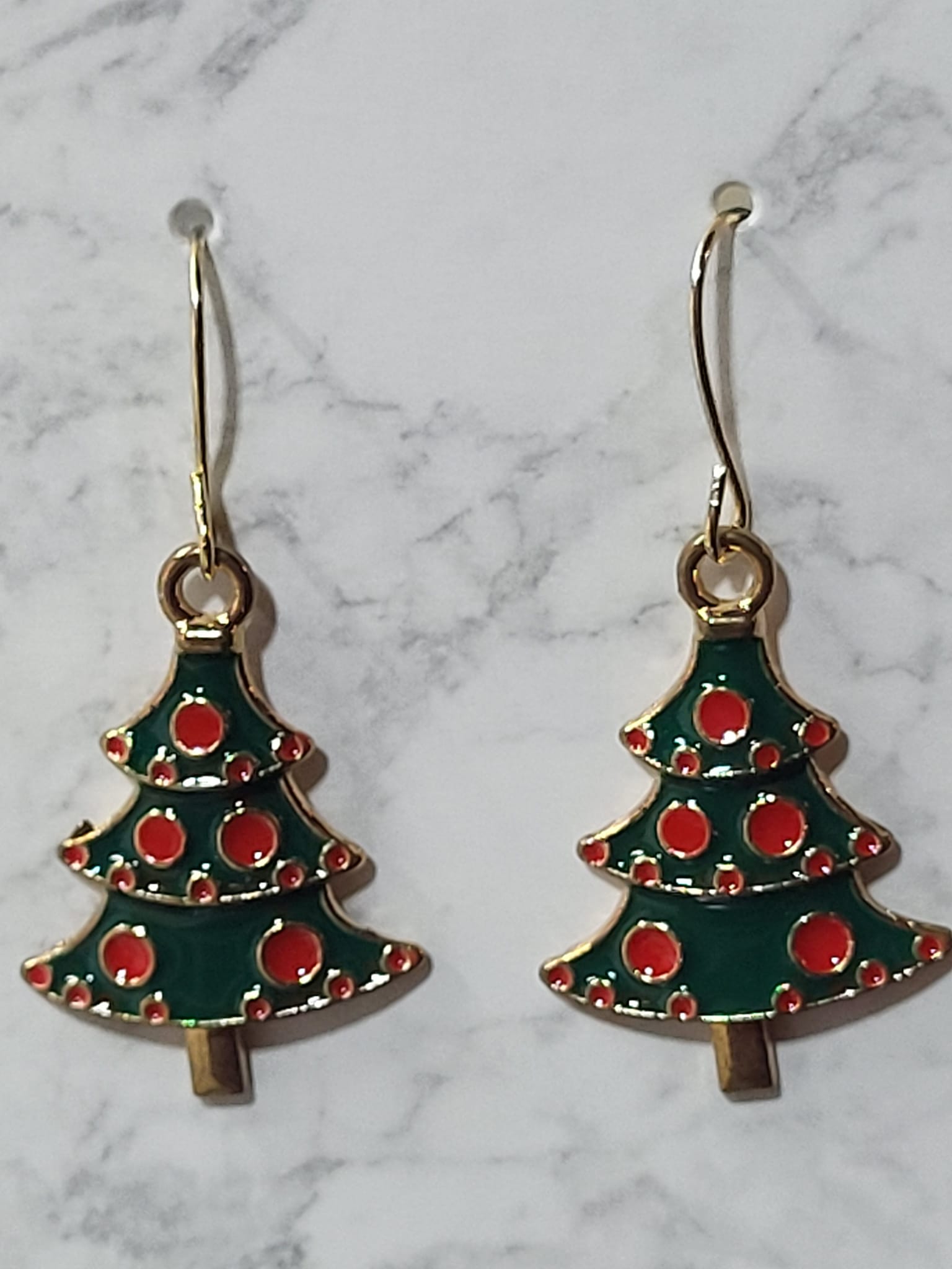 Green and red enamel Christmas tree charm dangle earrings with red ornament dots and gold tone outline on gold French wire on marble surface