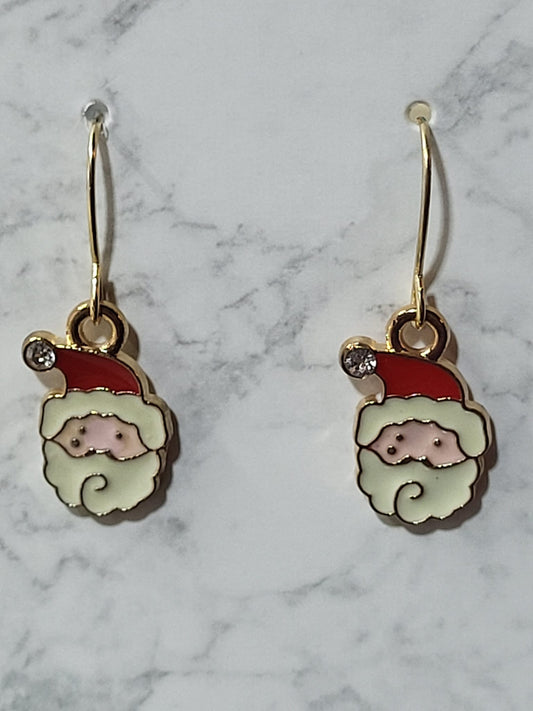 Enamel Santa face charm dangle earrings with red hat, white beard, rosy nose and crystal accent on gold French wire on marble surface