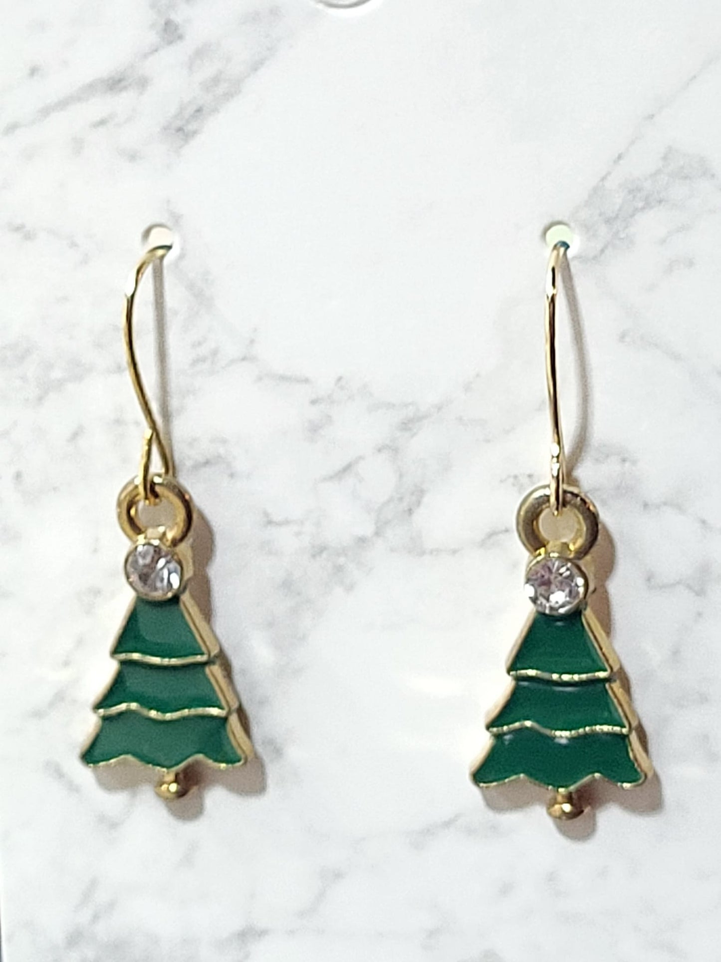 Green enamel Christmas tree dangle earrings with tiered layers, crystal rhinestone accent and gold tone outline on gold French wire on marble surface