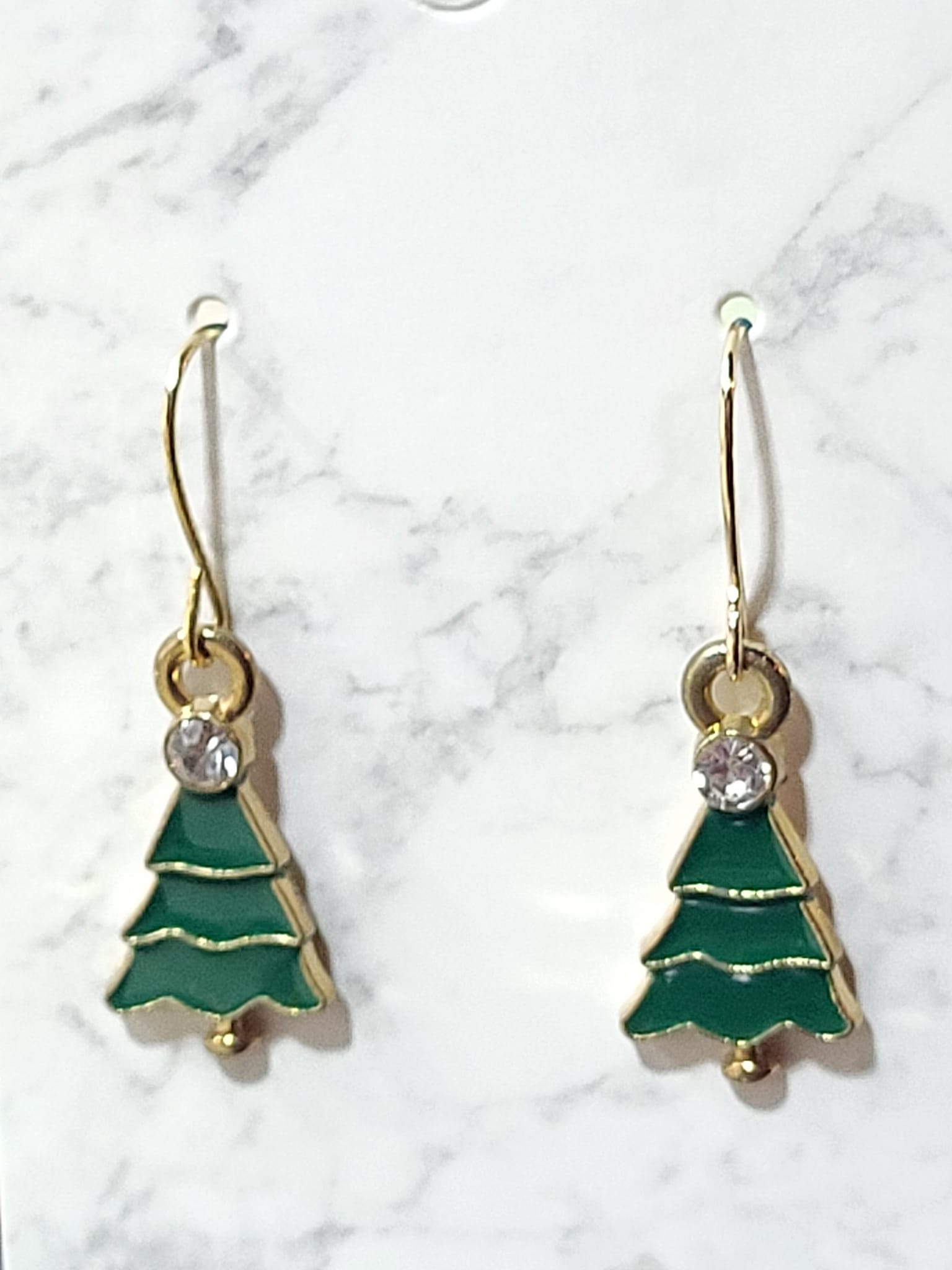 Green enamel Christmas tree dangle earrings with tiered layers, crystal rhinestone accent and gold tone outline on gold French wire on marble surface