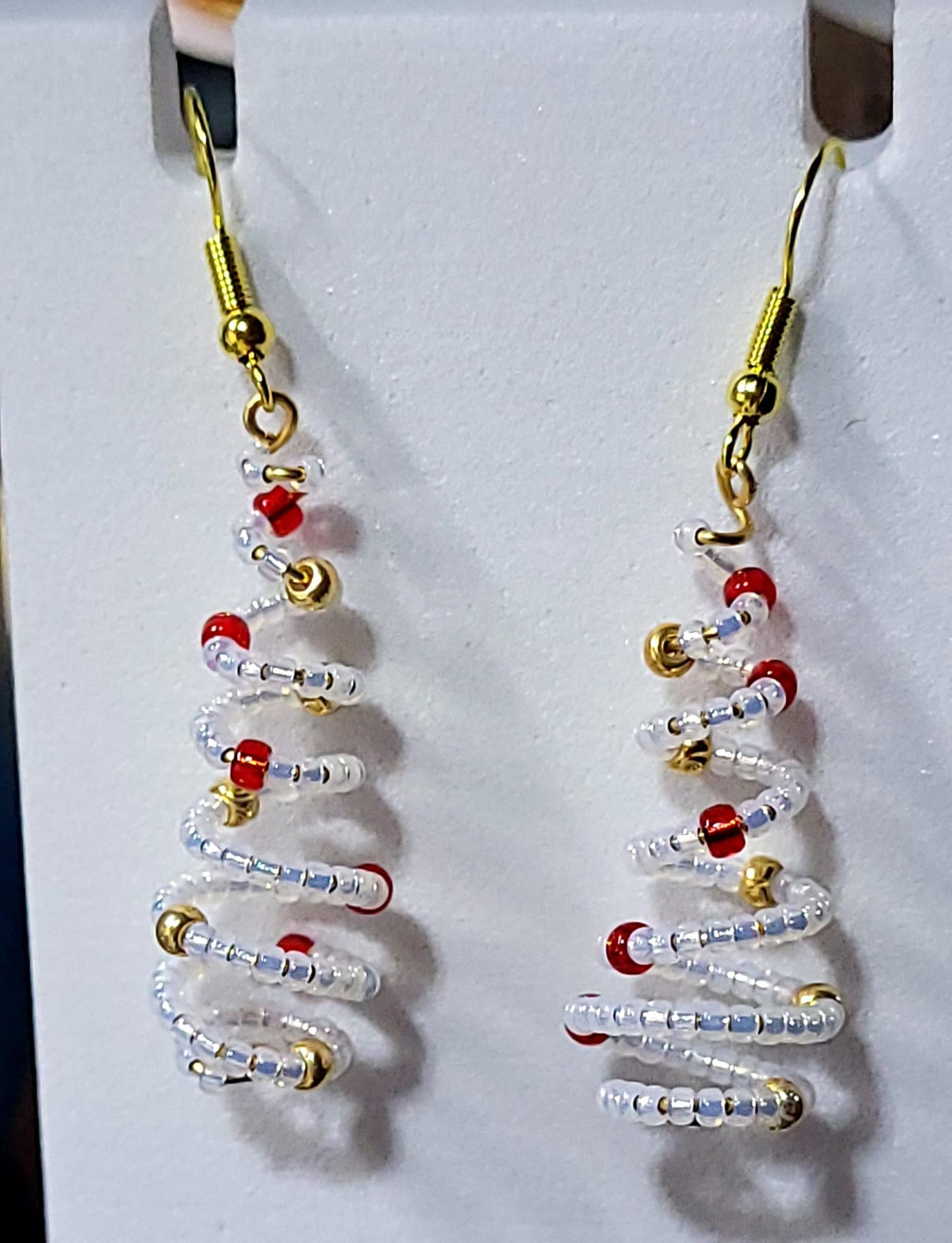 Handmade spiral wire Christmas tree earrings with clear white delica seed beads and red gold bead accents on gold French wire on white earring card