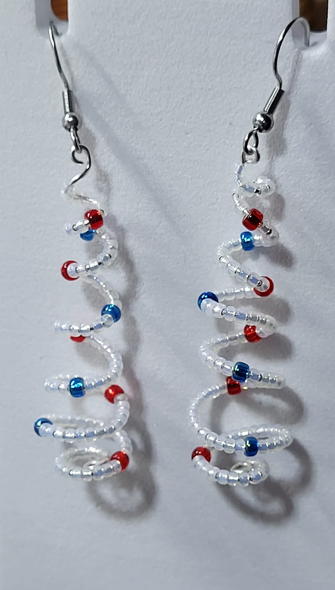 Handmade spiral wire Christmas tree earrings with clear white delica seed beads and red blue bead accents on silver French wire on white earring card