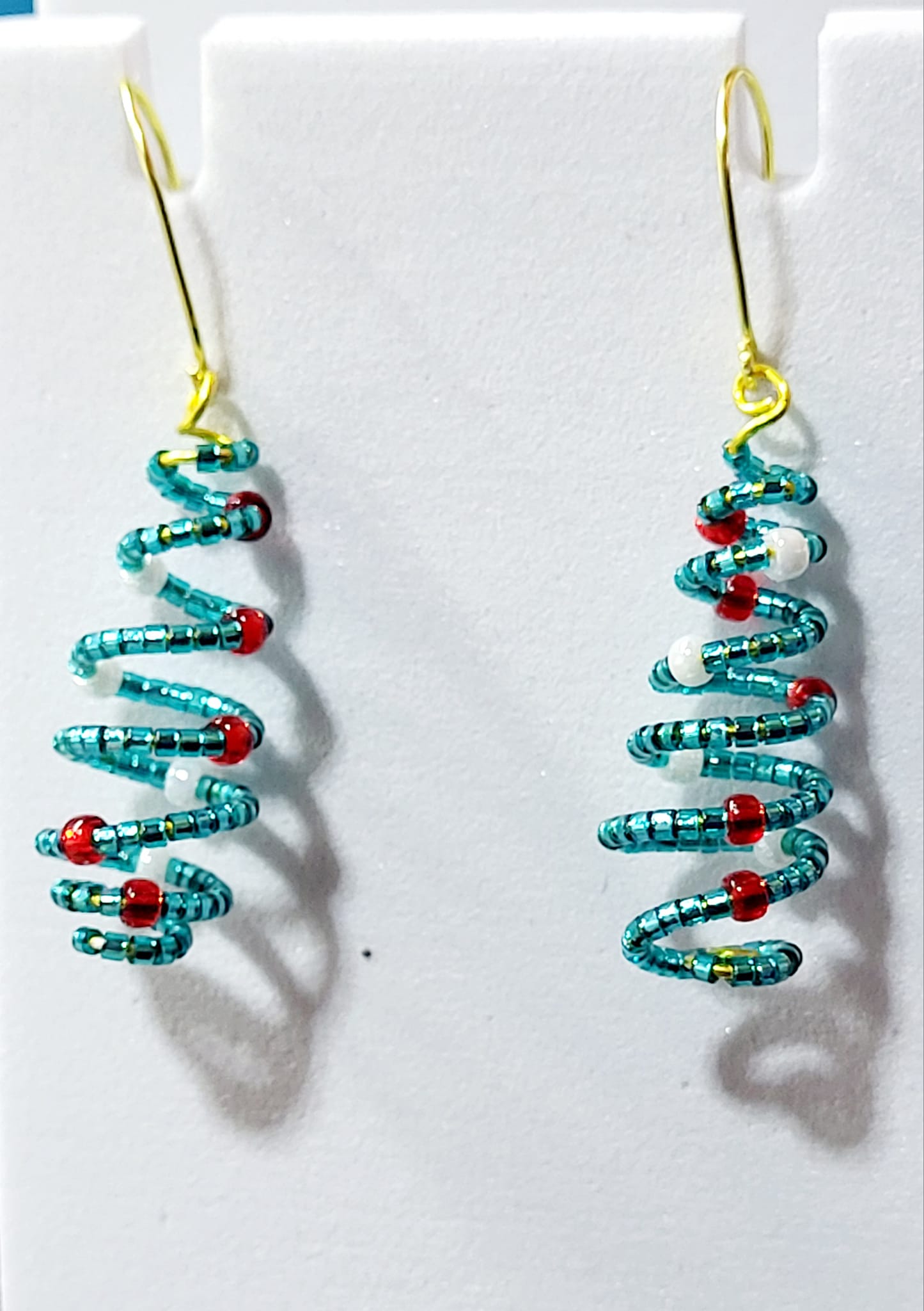 Handmade spiral wire Christmas tree earrings with teal turquoise delica seed beads and red white bead accents on gold French wire on white earring card