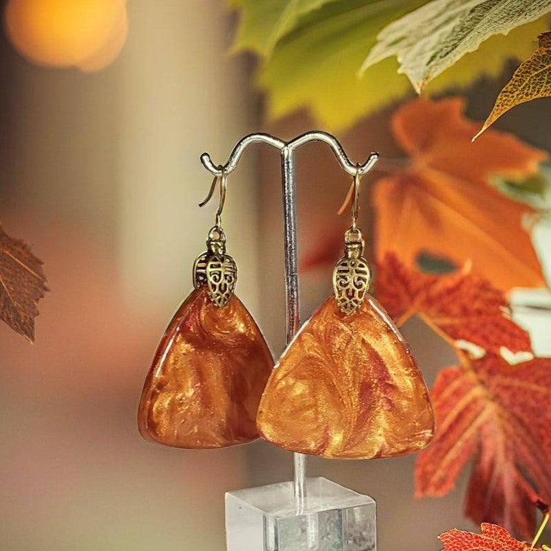 Pair of amber-colored earrings on a stand with autumn leaves in the background