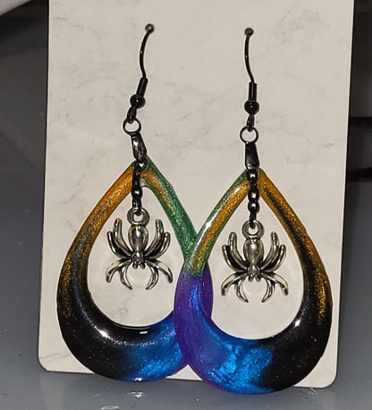 Multicolor resin open teardrop hoop earrings with gold green purple blue black gradient and dangling silver spider charm on marble display card