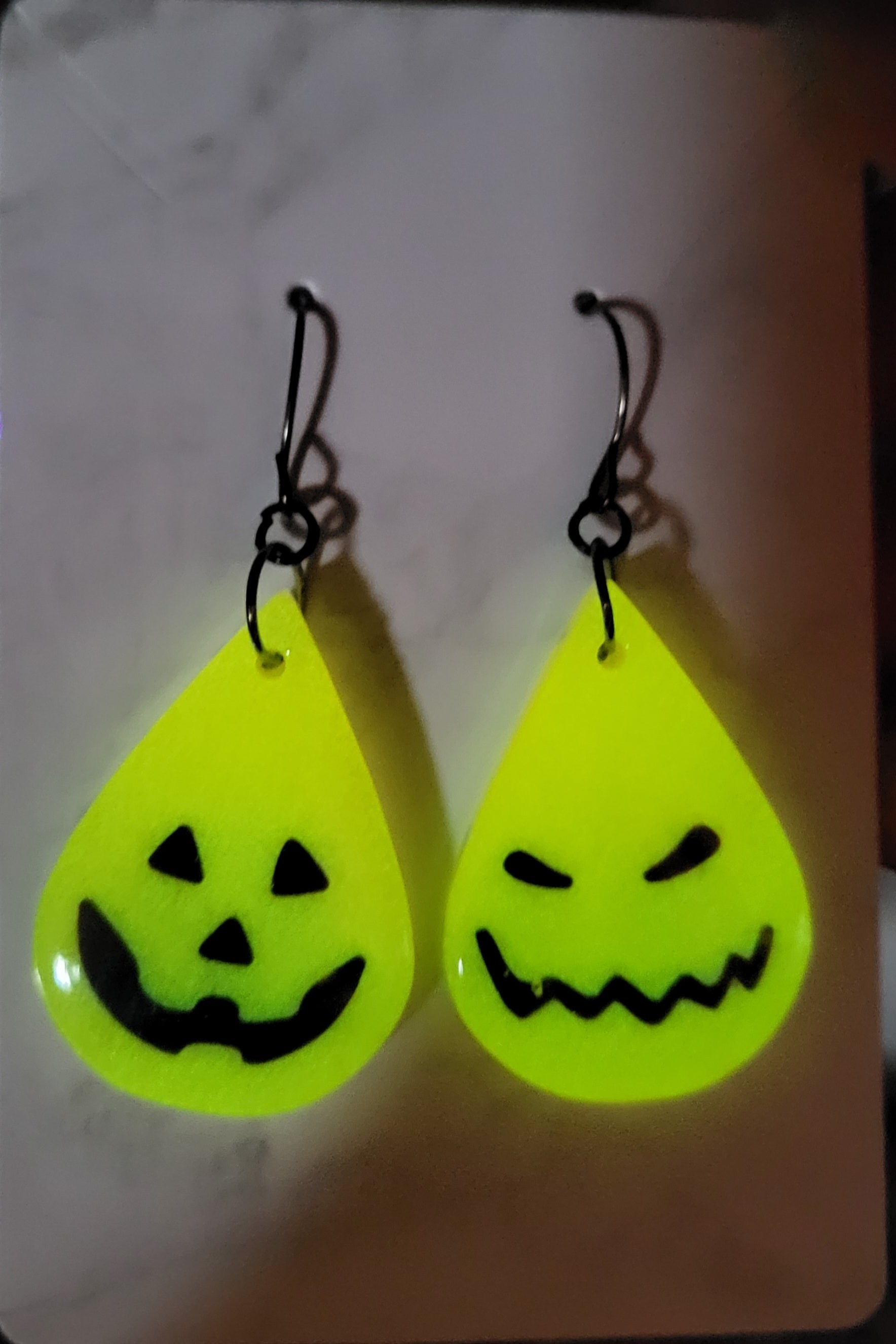 Mismatched jack-o-lantern resin teardrop earrings glowing neon green in the dark