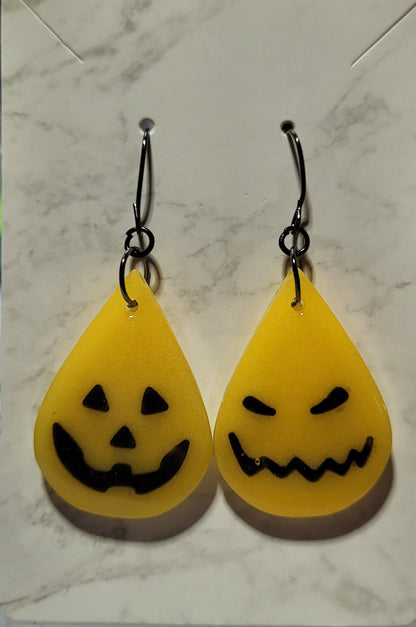 Pumpkin yellow jack-o-lantern resin teardrop earrings with mismatched faces on marble display card