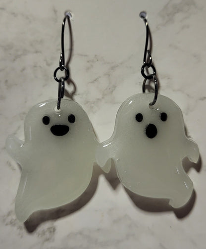 Chunky mismatched ghost glow in the dark resin earrings in daylight showing bright white resin with black facial features on marble surface
